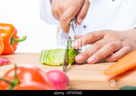 Cutting cucumber slices on a wooden board with a sharp knife close up Stock Photo