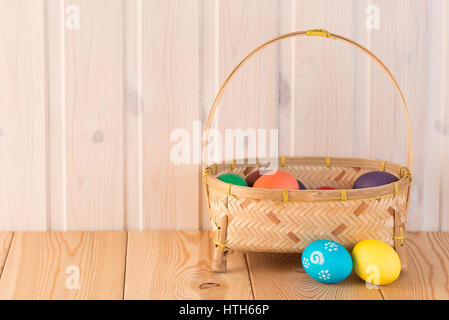 colored eggs in a straw basket on a wooden background Stock Photo