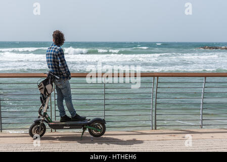 young man on electric scooter watching the sea, Tel Aviv-Yafo, Israel Stock Photo