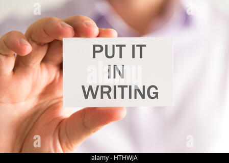 Closeup on businessman holding a card with PUT IT IN WRITING message, business concept image with soft focus background Stock Photo
