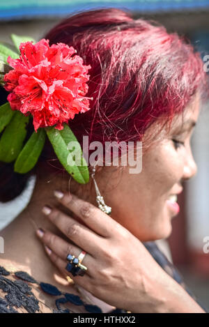 A woman wears a red rhododendron behind her ear.