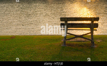 Vintage bench in public park with reflection of sunset on the lake effect, selective focus. Stock Photo
