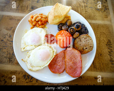 full English breakfast two fried eggs, bacon, baked beans, white toast, black pudding, grilled tomato, sausage and Ketchup Stock Photo