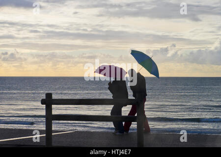 tourists with umbrellas during a rain shower on the promenade at Hardelot beah, Cote d'Opale, France