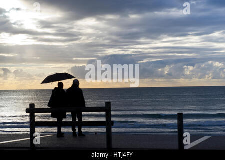 tourists with umbrellas during a rain shower on the promenade at Hardelot beah, Cote d'Opale, France
