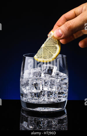 Glass glass of water with lemon on the dark background. Mountain mineral pure mountain water with gas bubbles and a lemon slice and spray tonic refres Stock Photo