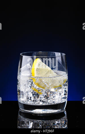 Glass glass of water with lemon on the dark background. Mountain mineral pure mountain water with gas bubbles and a lemon slice and spray tonic refres Stock Photo