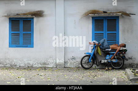 HO CHI MINH CITY, VIET NAM- APRIL 30, 2016: Vietnamese motorbike taxi driver circus when sleeping on motorcycle in dangerous at pavement, man set moto Stock Photo