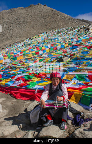 Tibetan nomad woman pilgrim sitting on rock, holding prayer beads in hand at Dolma La top en route Mt. Kailash Kora Stock Photo