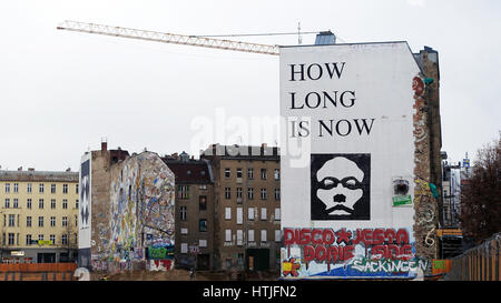 Famous 'How Long Is Now' mural on legendary Kunsthaus Tacheles building in Mitte neighborhood of Berlin stands in contrast with empty lot and crane. Stock Photo