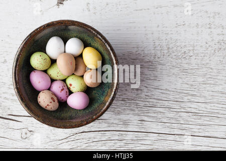 Sugar coated speckled easter eggs in ceramic bowl on white rustic wooden table. Top view with copy space Stock Photo