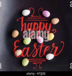 Happy Easter hand lettering calligraphy phrase on black background, decorated with sugar coated speckled easter eggs Stock Photo