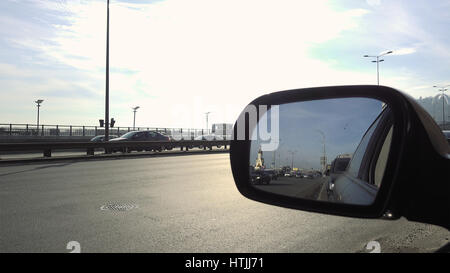 Rearview mirror of the car. View in rear view mirror of city street on the day rush hour traffic. Cars and vehicles on the road. Stock Photo