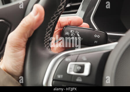 Driver hand pushing a headlights mode selector, modern crossover car interior details Stock Photo