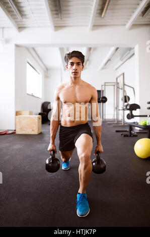 Fit hispanic man doing strength training, doing lunges with kettlebells in crossfit gym Stock Photo