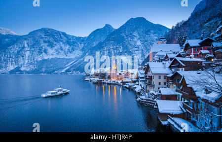 Classic postcard view of famous Hallstatt lakeside town in the Alps with traditional passenger ship on Hallstattersee in mystical winter twilight Stock Photo