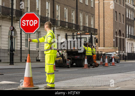 A brightly coloured workman in high vis clothing directing traffic on a quiet London Square