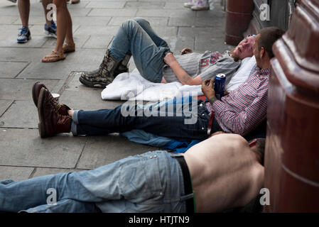 Men laying on the ground outside the Camden Town station; drinking beer Stock Photo