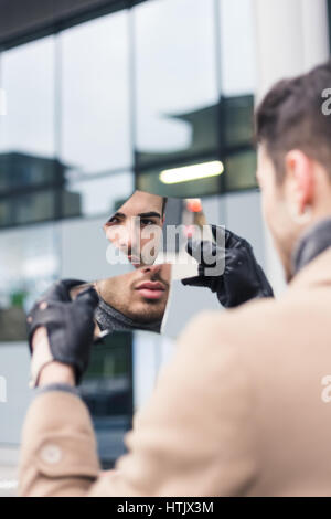 Beautiful young man with short hair looking at himself in a shattered mirror. Stock Photo