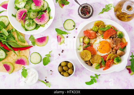 Fried eggs with vegetables - shakshuka and fresh salad cucumber, watermelon radish and arugula. Flat lay. Top view Stock Photo