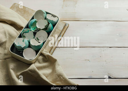 Plate full of blue tinted eggshells on white wooden table. Easter decoration. Stock Photo