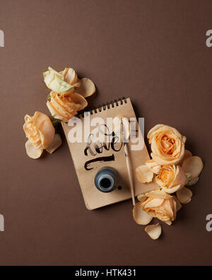 Notepad with written word Love and flowers on a brown background, flat lay Stock Photo