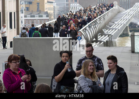 London Millenium Bridge filled with people crossing the Thames River on a busy sunny weekend in March 2017 Stock Photo