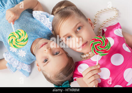 Two sisters lie the head to each other and hold in his hand a beautiful large candy Stock Photo