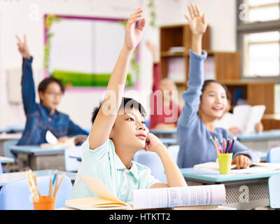 asian primary school pupils raising hands to answer questions in class. Stock Photo