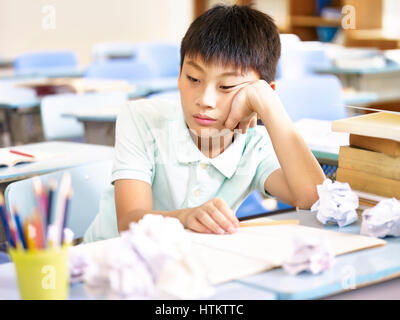 frustrated asian pupil sitting at desk dazing Stock Photo