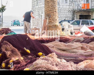 a fisherman mending sewing repairing his fishing net nets on the harbor harbour quayside Croatia Stock Photo