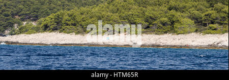 a lone single one sunbather alone on an isolated stony shingle rocky beach under the shade of a blue parasol umbrella in south Croatia Stock Photo