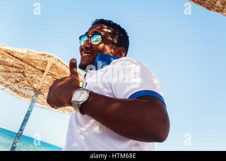 Arab young man in sunglasses and show gesture Class Pleases success and be proud of yourself, on the beach. Stock Photo