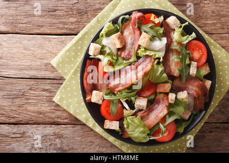 Spicy salad of bacon, tomato, croutons and lettuce close-up on a plate on a table. Horizontal view from above Stock Photo