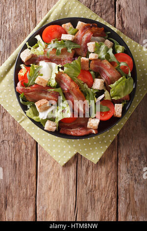 Spicy salad of bacon, tomato, croutons and lettuce close-up on a plate on a table. Vertical view from above Stock Photo