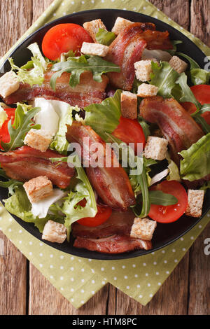 Salad of fried bacon, tomato, croutons and lettuce close-up on a plate on a table. Vertical view from above Stock Photo