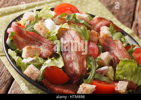 Spicy salad of bacon, tomato, croutons and lettuce close-up on a plate on a table. Horizontal Stock Photo