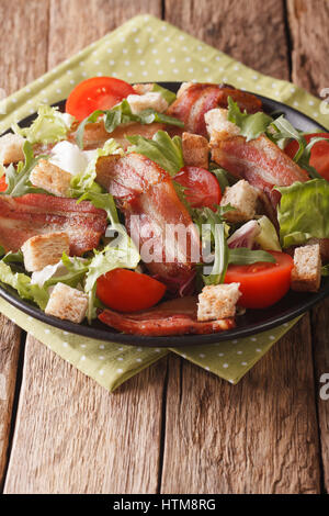 Salad of fried bacon, tomato, croutons and lettuce close-up on a plate on a table. vertical Stock Photo
