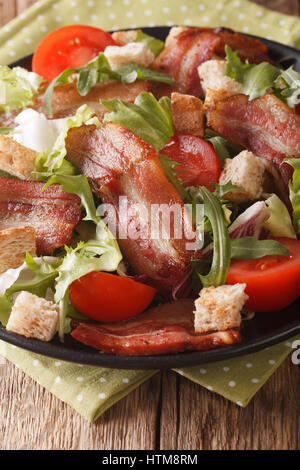 Spicy salad of bacon, tomato, croutons and lettuce close-up on a plate on a table. vertical Stock Photo