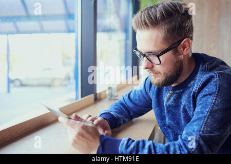 A freelance hipster man with  tablet in his hand works cafe by the window. Stock Photo