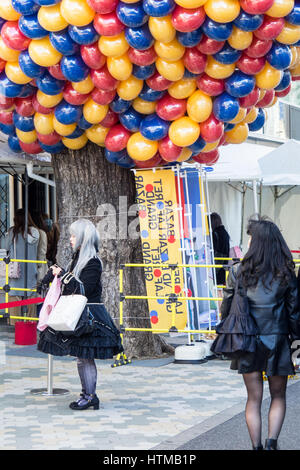A Japanese girl in cosplay standing under a large cluster of blue red and yellow ballons. Stock Photo
