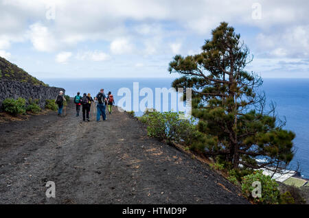 Hiking trail, Fuencaliente.  La Palma.  Tourist hikers walking along a volcanic road on their guided hike in the Fuencaliente region of La Palma.  A Canarian pine tree is able to grow on the steep mountain sides or the volcano ridge. Stock Photo