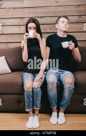shy guy flirts with the girl. They are sitting on a brown sofa at home. The concept of the first love relations Stock Photo