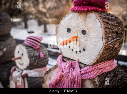 Close up of a nose of a snowman made of wooden log wearing purple and pink hat and scarf Stock Photo