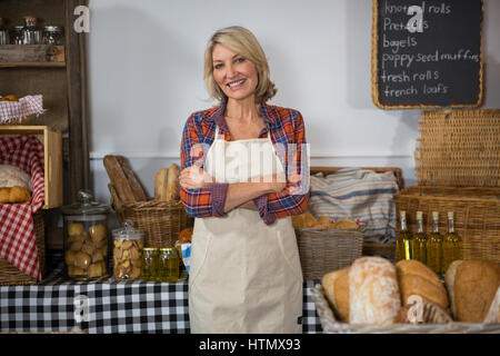 Portrait of smiling female staff standing with arms crossed at counter in bakery shop Stock Photo