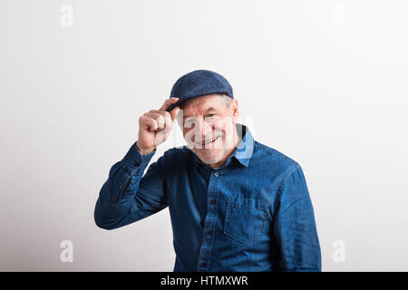 Senior man in denim shirt and flat cap smiling, studio shot. Stock Photo