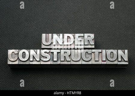 under construction phrase made from metallic letterpress blocks on black perforated surface Stock Photo