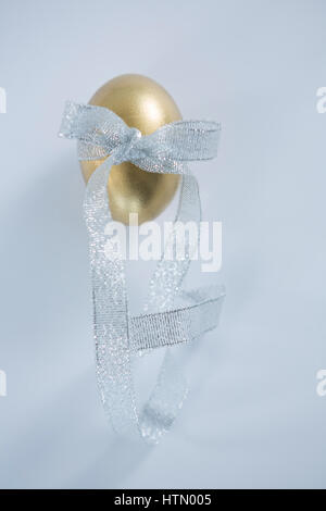 Close-up of golden Easter egg tied with ribbon on white background Stock Photo