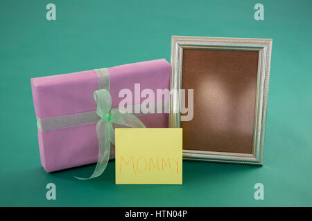 Close-up of gift box, photo frame with text mom on card against green background Stock Photo