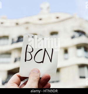 closeup of the hand of a young caucasian man holding a note with the word BCN, for Barcelona, written in it, in front of La Pedrera, in Barcelona, Spa Stock Photo
